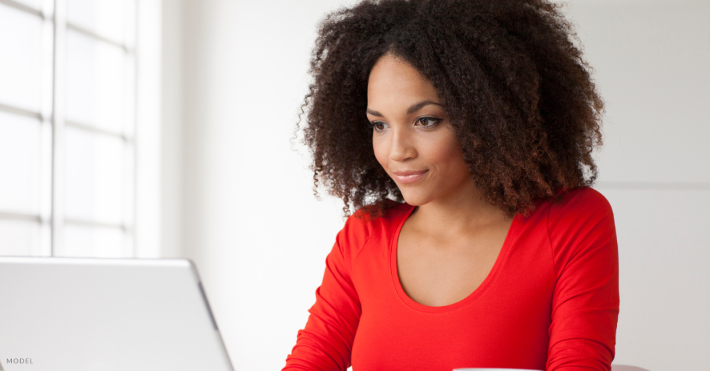 A woman in a red shirt looking at her computer (model).