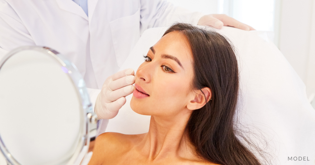 A woman looking in mirror at plastic surgeon's practice (model)