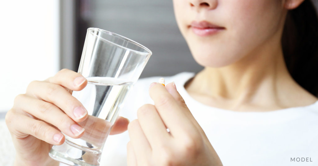 A woman looking at medicine and holding a glass of water (model)