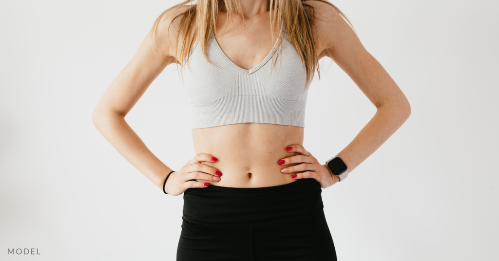 A woman wearing a sports bra and workout clothes exposing her stomach (model)