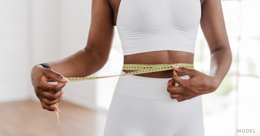 A woman measuring her waist, wearing a work-out outfit (model)