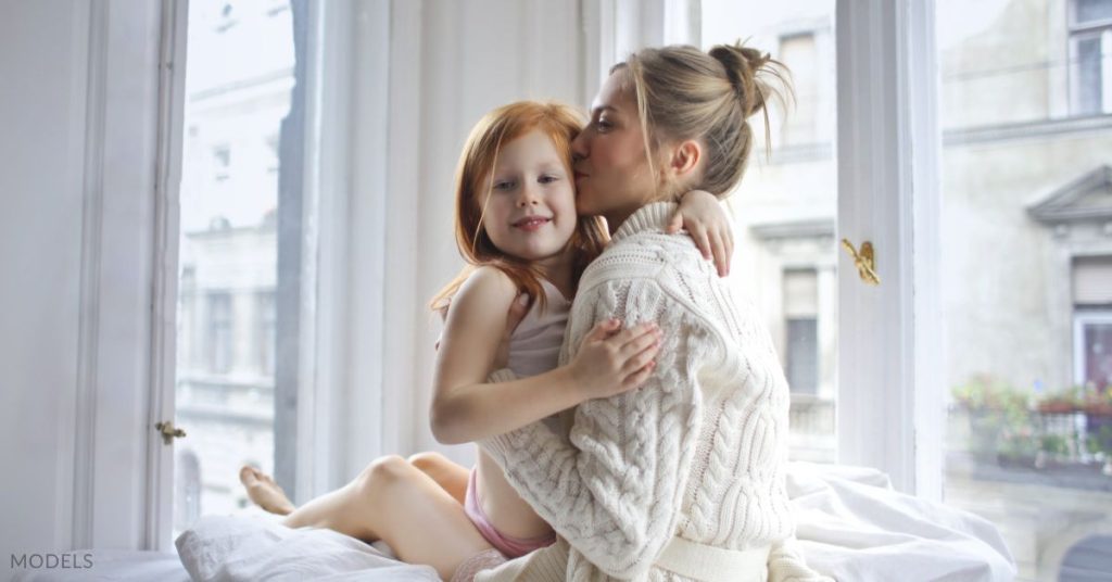 A mother and daughter sitting on a bed together. (model)