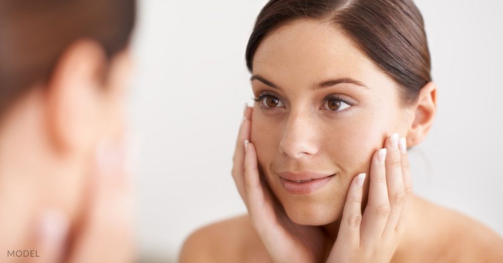 A woman looking at her face in the mirror (model)