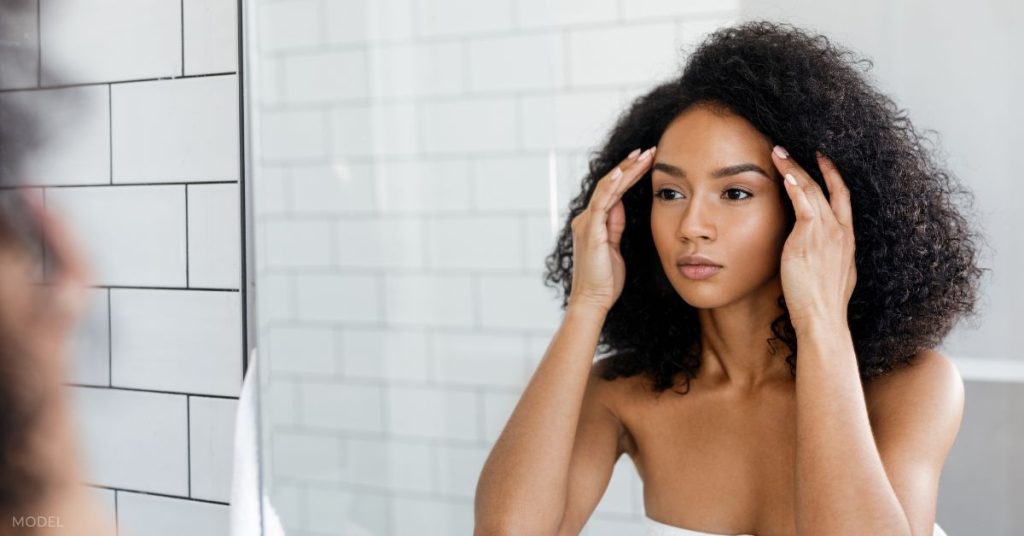 A woman looking at her skin in the mirror (model)