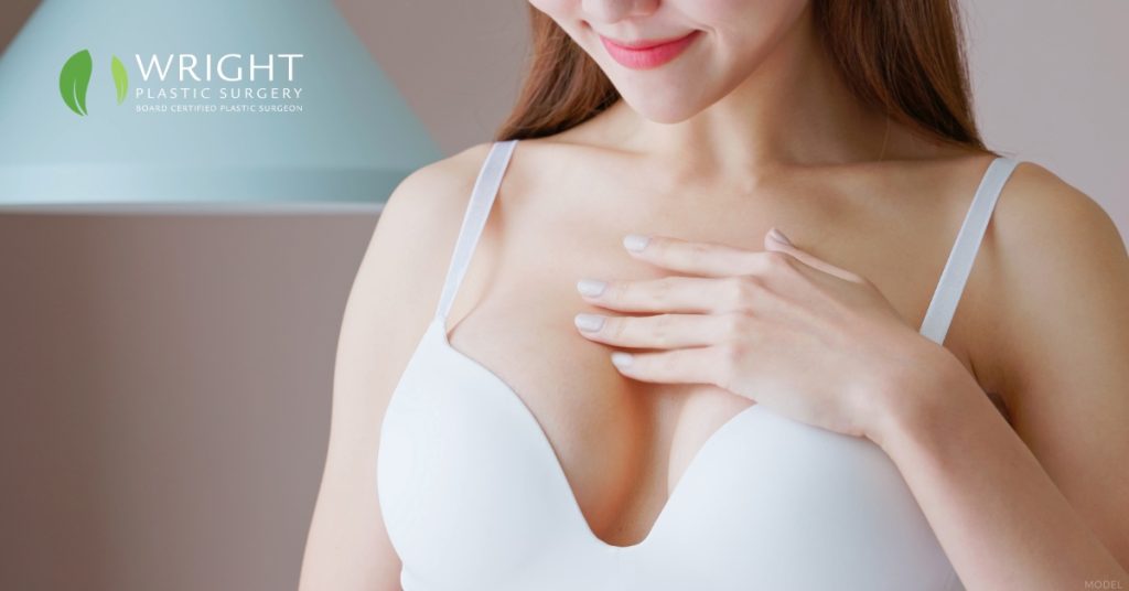 Woman touching her chest after breast augmentation surgery (model) Wright Plastic Surgery and Med Spa Logo