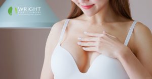 Woman touching her chest after breast augmentation surgery (model) Wright Plastic Surgery and Med Spa Logo
